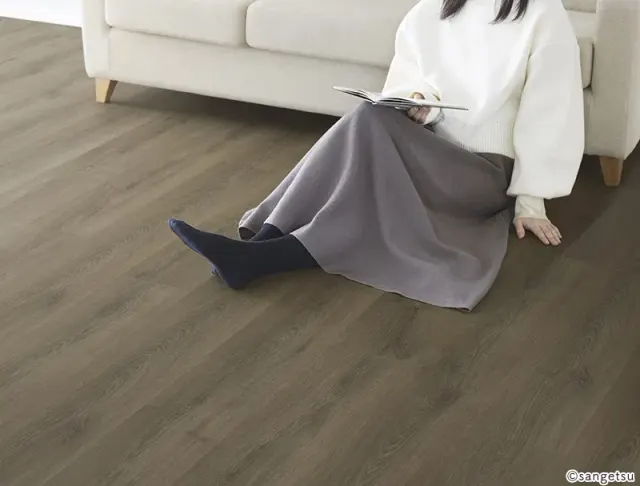 Phòng khách lát sàn vân gỗ nâu xám, người ngồi đọc sách trên sàn cạnh ghế sofa trắng, mã MF106