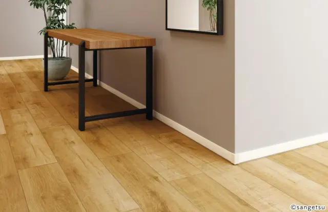 Len chân tường nhựa màu trắng mảnh chạy quanh góc lồi của tường màu xám, sàn vân gỗ, bàn gỗ chân sắt