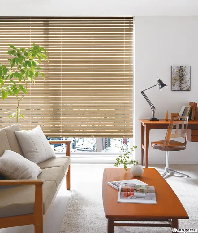 Phòng khách có cửa sổ lớn treo rèm gỗ màu gỗ sáng, sofa khung gỗ đệm be, bàn làm việc nhỏ và cây xanh, mã WB117